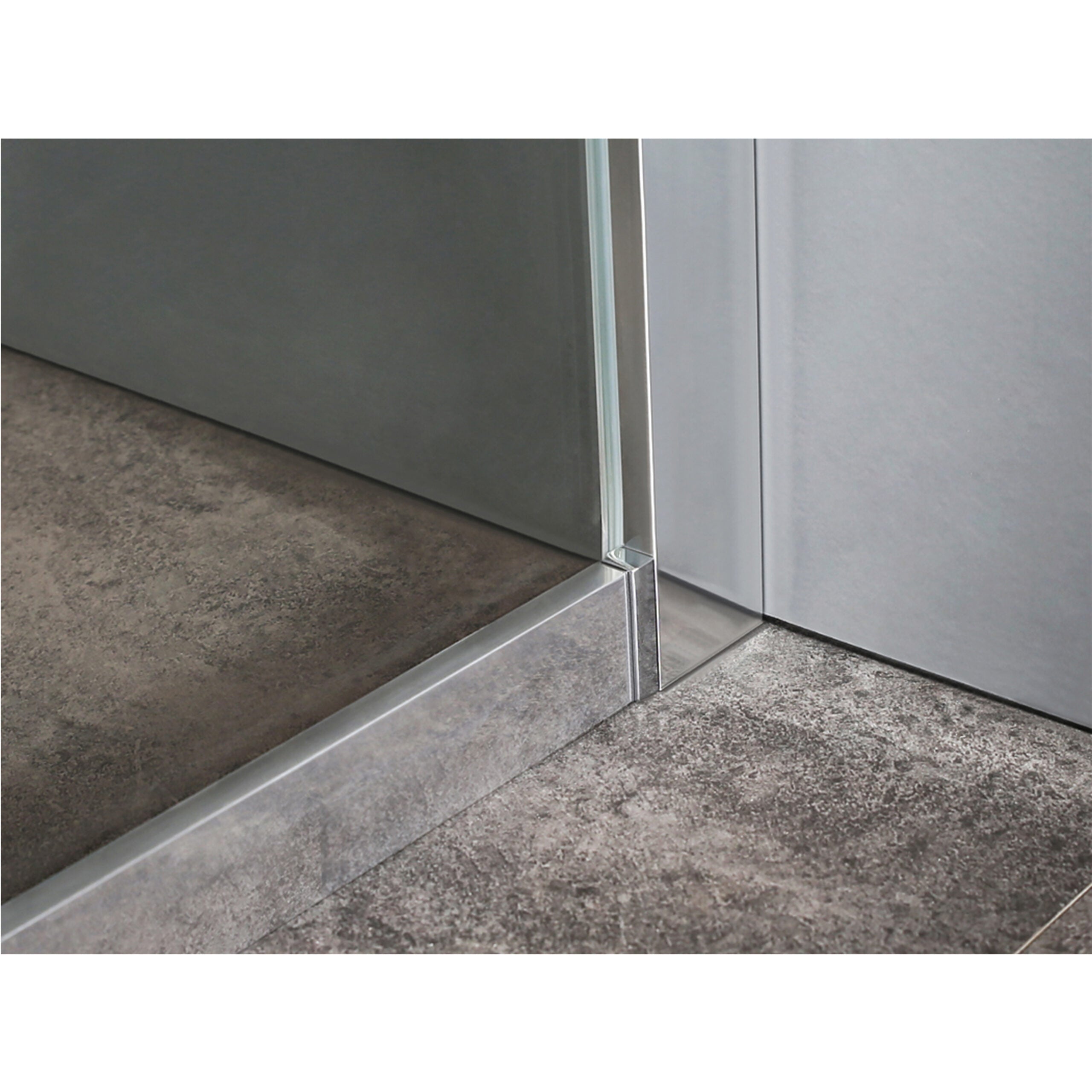 Close-up van een douchewandprofiel in chroomkleur, strak gemonteerd op een grijze tegelvloer.